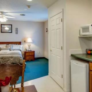 A cozy hotel room featuring a bed, nightstand with a lamp, and a small kitchenette area.