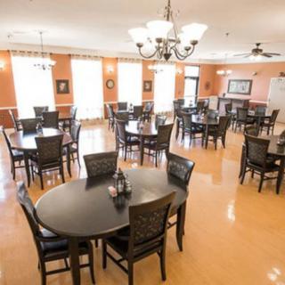 A well-lit dining area with multiple tables and chairs, featuring elegant chandeliers and wooden floors.
