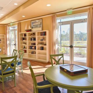 A cozy library interior with bookshelves, tables, and chairs bathed in sunlight.