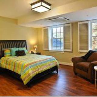 A cozy bedroom with a colorful bedspread, a comfortable armchair, and large windows letting in natural light.