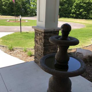 A small fountain on a sunny day in a landscaped yard.
