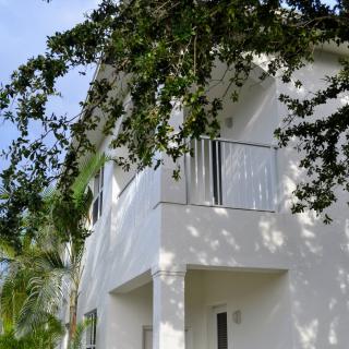A white house with a balcony and trees casting shadows.