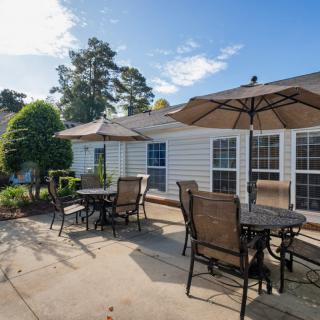 A sunny backyard patio with tables, chairs, and umbrellas.