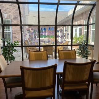 A stylish dining area with wooden furniture and indoor plants under a glass ceiling, flooded with natural light.