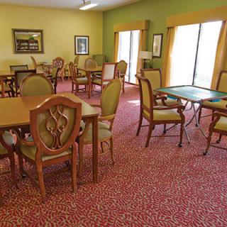 A well-lit dining room with several tables and chairs arranged on a patterned carpet.