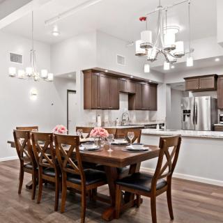 A modern open-concept dining room and kitchen with wooden furniture and elegant chandeliers.