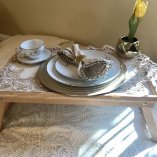 A cozy breakfast setup with a decorative tray featuring elegant dishware and a single yellow tulip in a vase.