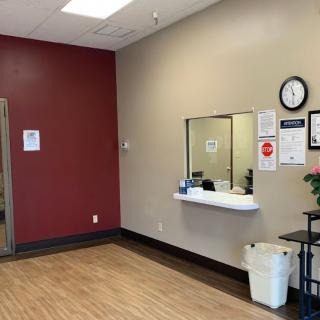 A simple waiting room with a reception window, wall clock, and waste bin.