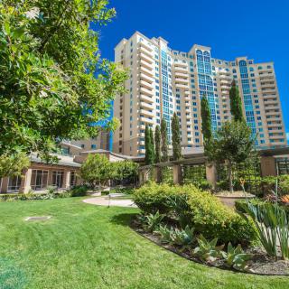 A high-rise apartment building surrounded by lush gardens and greenery on a clear day.