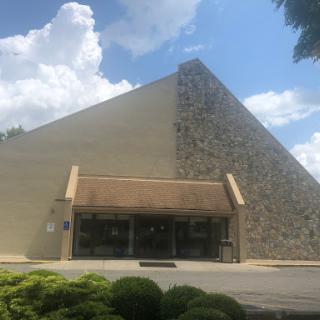 A uniquely designed building featuring a pyramid-like structure against a backdrop of fluffy clouds.