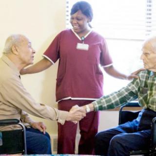 Two elderly individuals sharing a handshake, accompanied by a caregiver in a nursing home setting.