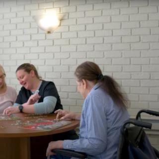 A caregiver interacts with elderly individuals in a nursing home setting.