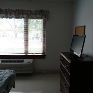 A simple bedroom featuring a dresser, television, and a large window allowing natural light.