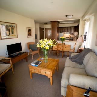 A cozy living room with a sofa, coffee table, and a view into the kitchen area, adorned with fresh flowers for a homely touch.