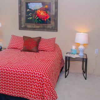 A cozy bedroom with a red patterned bedspread, a stylish nightstand with lamps, and artwork on the wall.