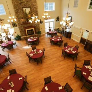 A spacious dining area with round tables and chairs, featuring a wooden floor and a grand fireplace.