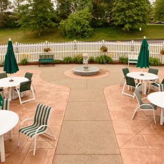 A serene outdoor seating area featuring tables and chairs with green umbrellas, surrounded by lush greenery.