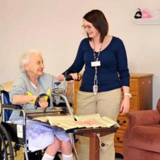A caregiver assisting an elderly woman in a wheelchair.