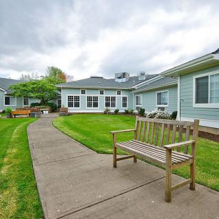 A wooden bench along a pathway in front of a building with a well-maintained lawn under a cloudy sky.