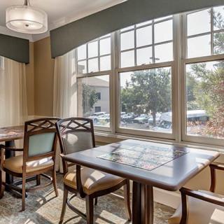 A well-lit dining area with wooden tables and chairs, featuring large windows that let in plenty of natural light.