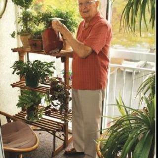 A senior man waters his indoor plants on a balcony.