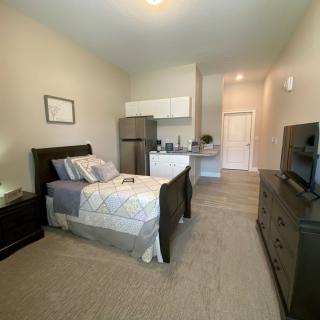 A cozy studio apartment with a single bed, kitchenette, and dresser.