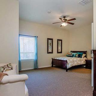 A spacious bedroom with a cozy bed, carpeted floor, and a ceiling fan.