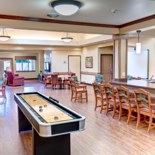 A spacious recreation room featuring a shuffleboard table, with ample seating and wooden flooring.