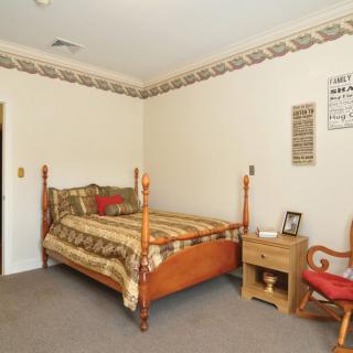 A traditional-style bedroom featuring a bed with patterned bedding, a wooden nightstand, and an upholstered chair.