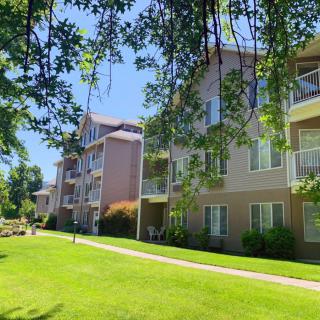 A view of apartment buildings surrounded by green lawns and trees under a clear blue sky.