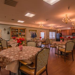 A cozy dining room with multiple tables and chairs, warmly lit with chandeliers.