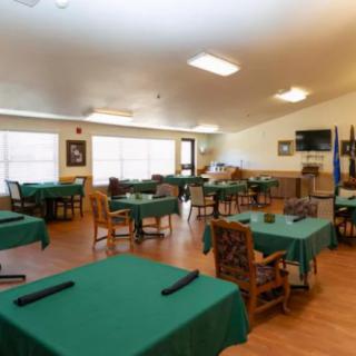 An indoor dining area with several tables covered in green tablecloths and wooden chairs arranged neatly.
