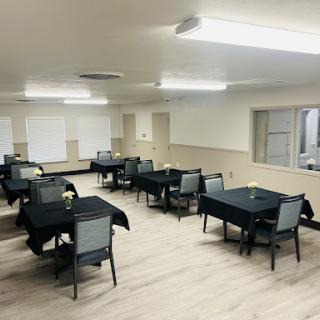 A spacious dining area with neatly arranged tables and chairs, featuring black tablecloths and bright overhead lighting.