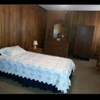 A modest bedroom with wood-paneled walls, featuring a single bed and a dresser with a mirror.