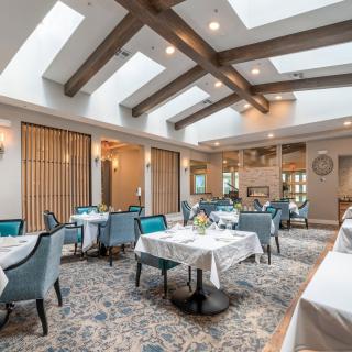 An elegant dining area featuring tables with white tablecloths, comfortable chairs, and natural light from skylights.