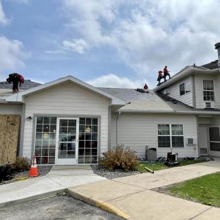 A house with workers on the roof under a cloudy sky.