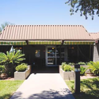 A welcoming entrance to a well-maintained building, surrounded by lush greenery and palm plants.