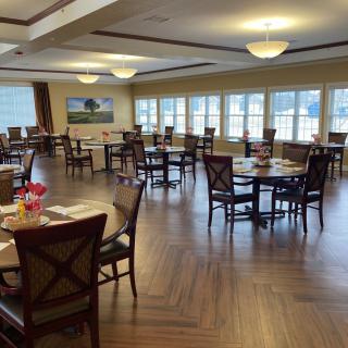 A spacious dining area with wooden tables and chairs, well-lit by large windows.