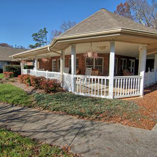 A cozy house with a wraparound porch, surrounded by a well-maintained garden and walkway during autumn.