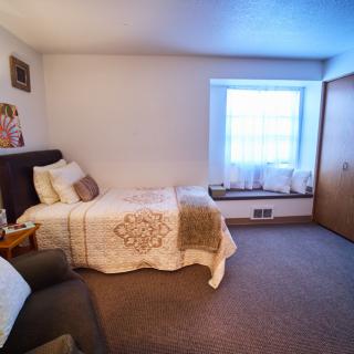 A cozy bedroom with a single bed and a large window letting in natural light.