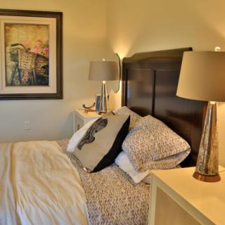 A cozy bedroom with a neatly made bed, stylish lamps, and elegant artwork.