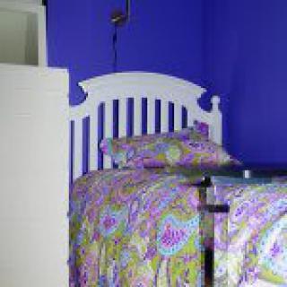 A bedroom with a white headboard and colorful paisley-patterned bedding against a vibrant purple wall.