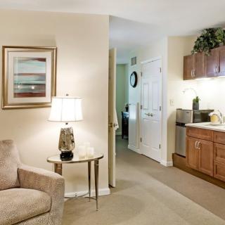 Cozy living room with a sofa, side table and lamp, leading to a kitchenette area.