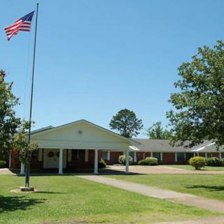 A building with an American flag on a pole, surrounded by a lawn and trees under a clear sky.