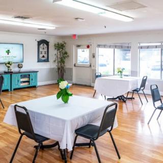 A bright dining room with neatly arranged tables and chairs, featuring white tablecloths and flower arrangements.