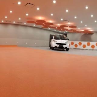 A sleek car parked in a modern interior with an orange flooring design and unique ceiling lights.