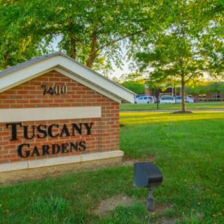 Entrance sign for Tuscany Gardens surrounded by trees and grass.
