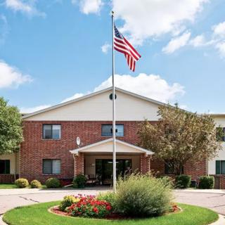 A building with an American flag flying in front of a landscaped entrance under a partly cloudy sky.