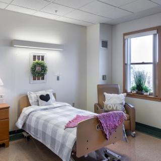 A cozy and well-lit hospital room featuring a patient bed, comfortable chair, and decorative touches.