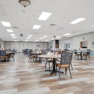An empty dining hall with several tables and chairs arranged neatly under bright, overhead lighting.